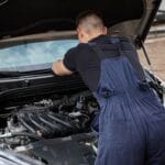 Mechanik naprawiający silnik samochodowy na zewnątrz w słoneczny dzień